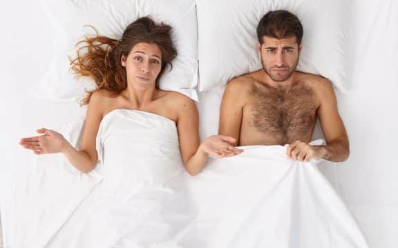 overhead shot of puzzled woman and her husband have sex problems in bed displeased expressions lie under white blanket man has impotence erection failure daylife family troubles concept 576x360